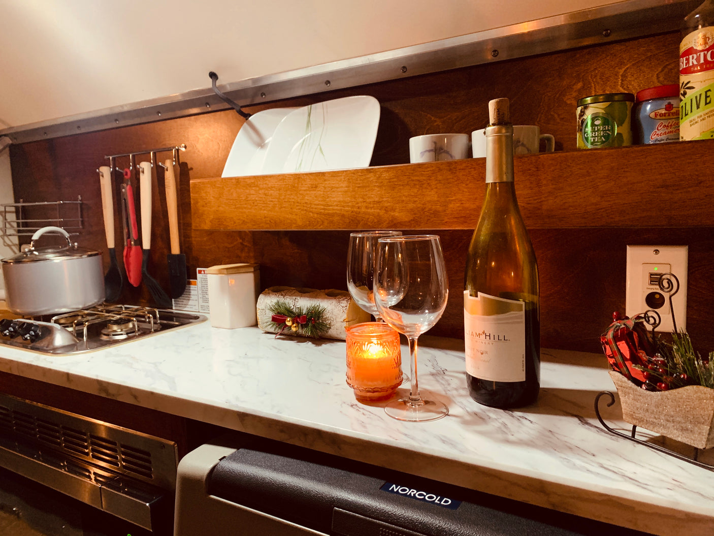Cozy kitchen setup in an RV rental, complete with a two-burner stove, wine glasses, and festive holiday decor.