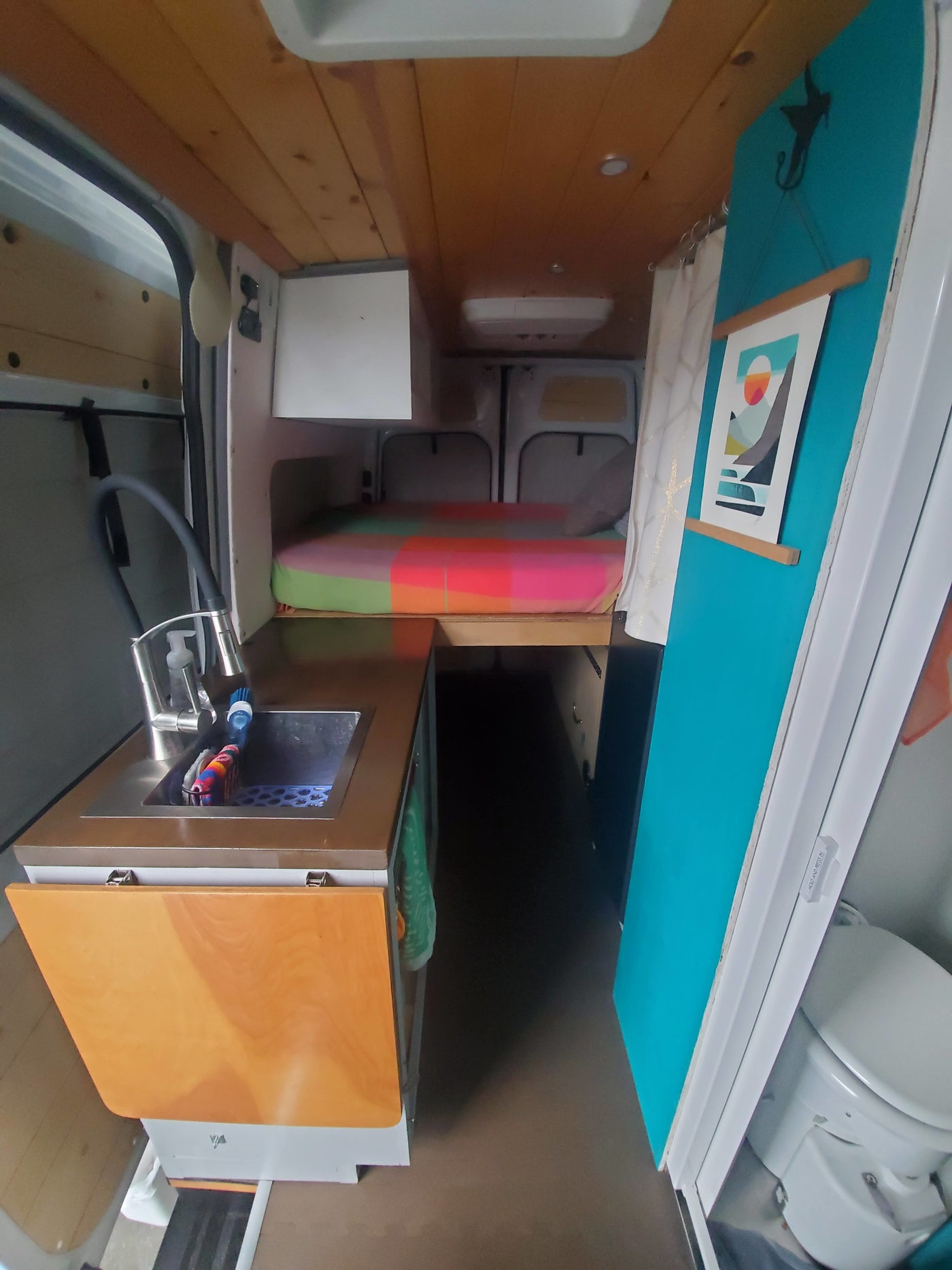 This RV rental's interior features a compact kitchen with sink, vibrant striped bed, and a toilet for travel. — photo 10