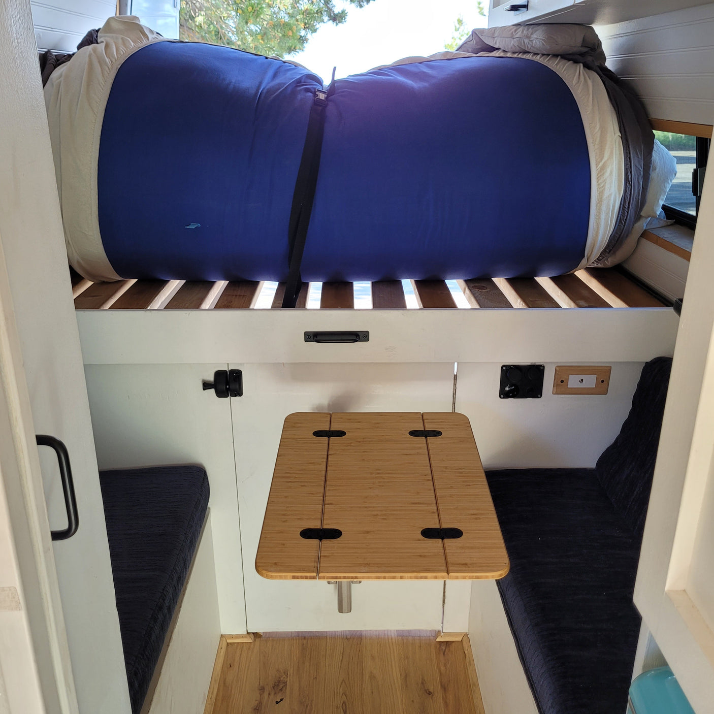 Inside a compact RV rental: a rolled-up bed, bamboo table, and bench seating.