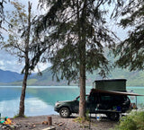 Scenic lakefront RV rental truck camping with a rooftop tent. Mountains and a campfire set the scene for wilderness adventure.