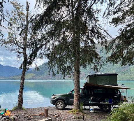 Scenic lakefront RV rental truck camping with a rooftop tent. Mountains and a campfire set the scene for wilderness adventure.