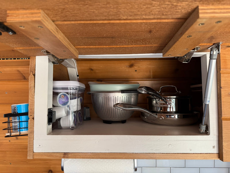 Open kitchen cabinet in an RV rental, showing organized coffee pods, colander, and Cuisinart cookware. — photo 20