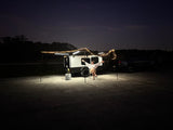 Woman relaxes under string-lit RV rental awning at night. This compact camper setup offers comfort for outdoor adventures.