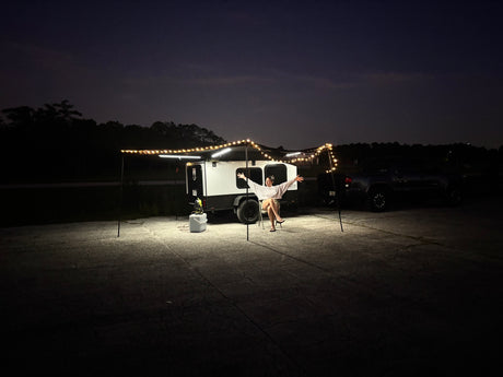 Woman relaxes under string-lit RV rental awning at night. This compact camper setup offers comfort for outdoor adventures.