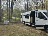 White rv rental camper van parked at a rustic campsite with a picnic table and fire pit, ideal for outdoor adventure.