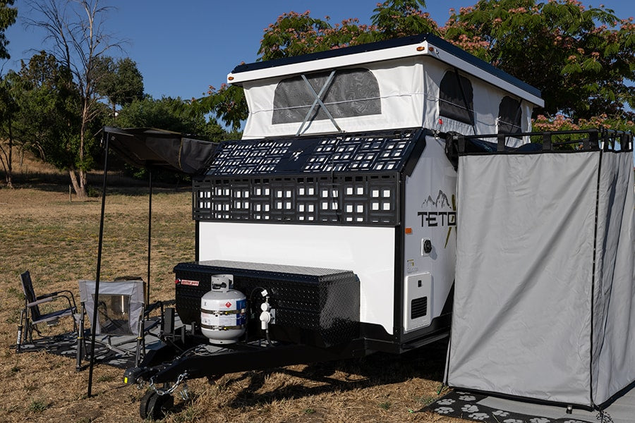 Explore off-grid with this compact RV rental. Pop-top travel trailer set up for camping, featuring an awning and privacy tent. — photo 14
