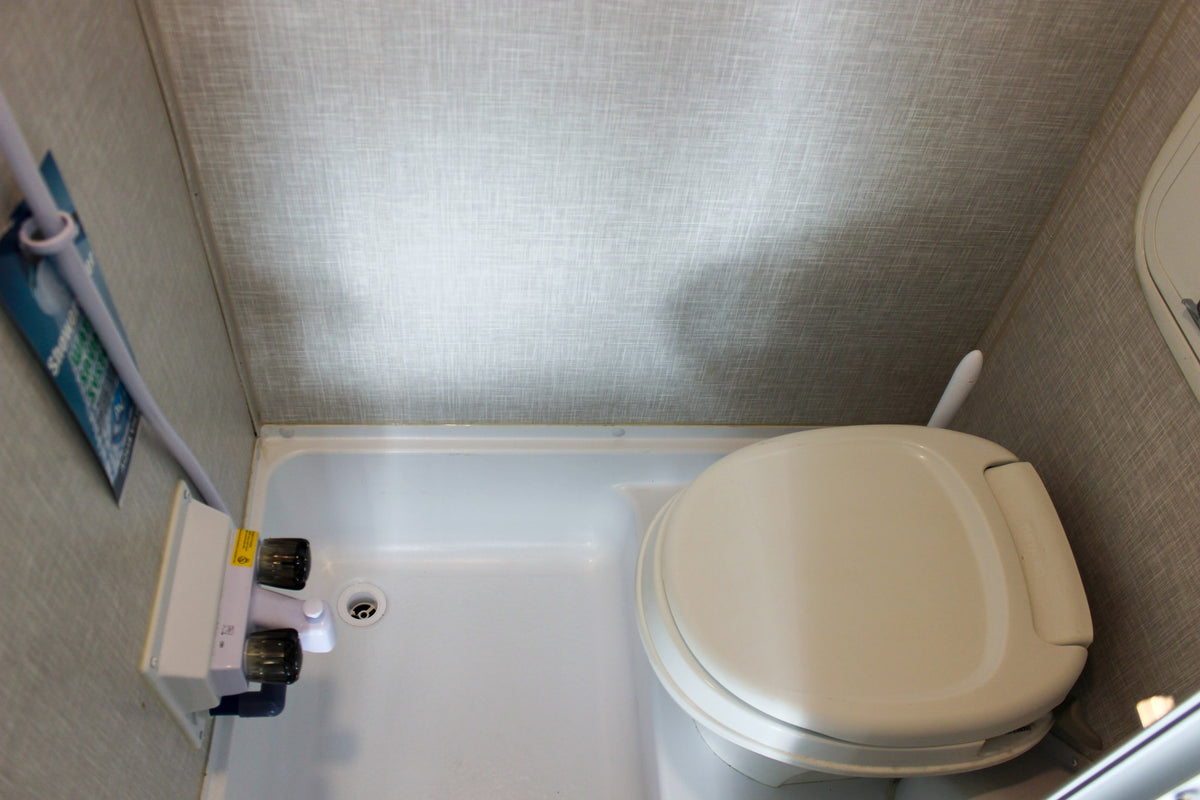 A compact RV rental bathroom showing a white toilet, shower pan, and shower controls on textured walls. — photo 20