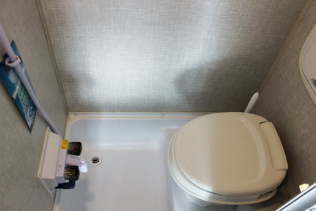 A compact RV rental bathroom showing a white toilet, shower pan, and shower controls on textured walls.
