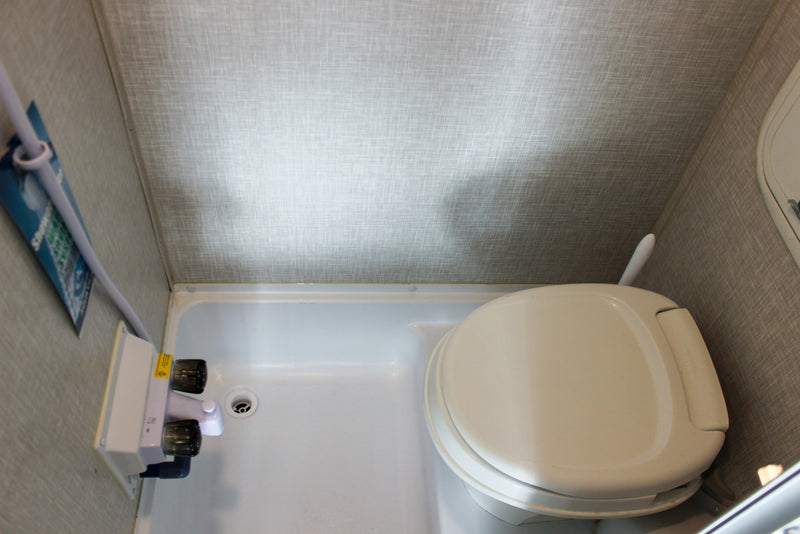 A compact RV rental bathroom showing a white toilet, shower pan, and shower controls on textured walls. — photo 20