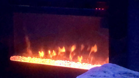 Cozy RV rental interior featuring an electric fireplace with glowing orange flames & white embers. A blue mound rests nearby.