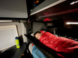 Cozy night in an RV rental! A boy rests in a bunk bed, his green water bottle on the table.