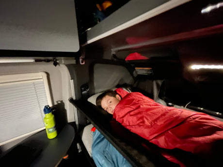Cozy night in an RV rental! A boy rests in a bunk bed, his green water bottle on the table.