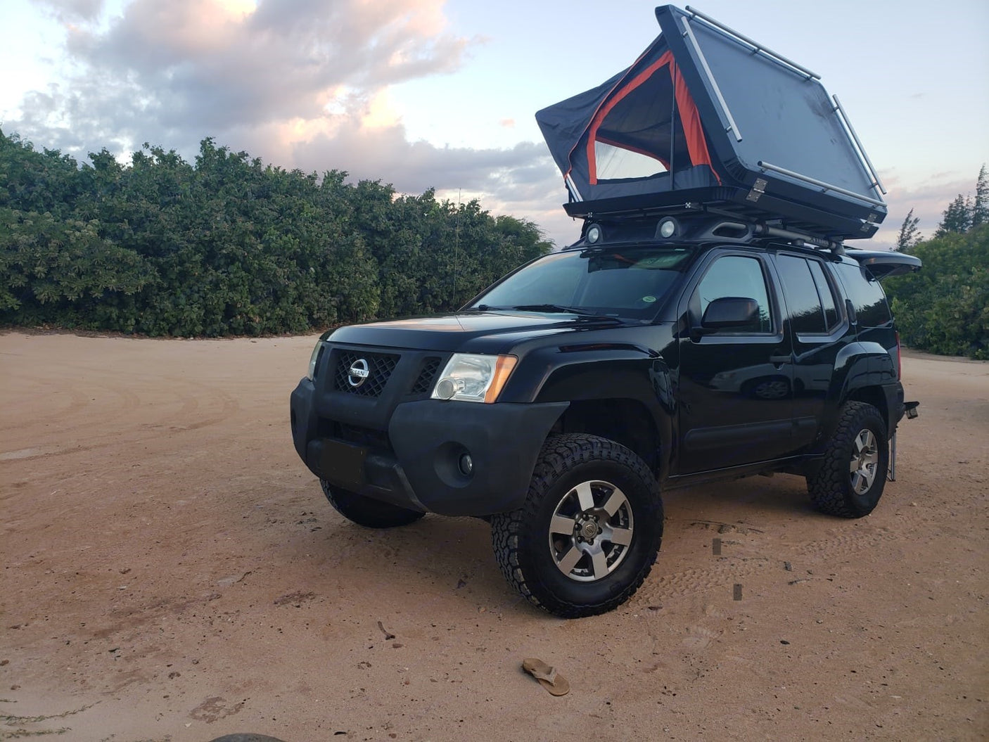 This black Nissan Xterra, an RV-style rental, with a deployed rooftop tent for off-road camping on sand.