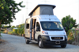 White pop-top camper van on a gravel road, ready for RV rental adventures, with open side door and natural surroundings.