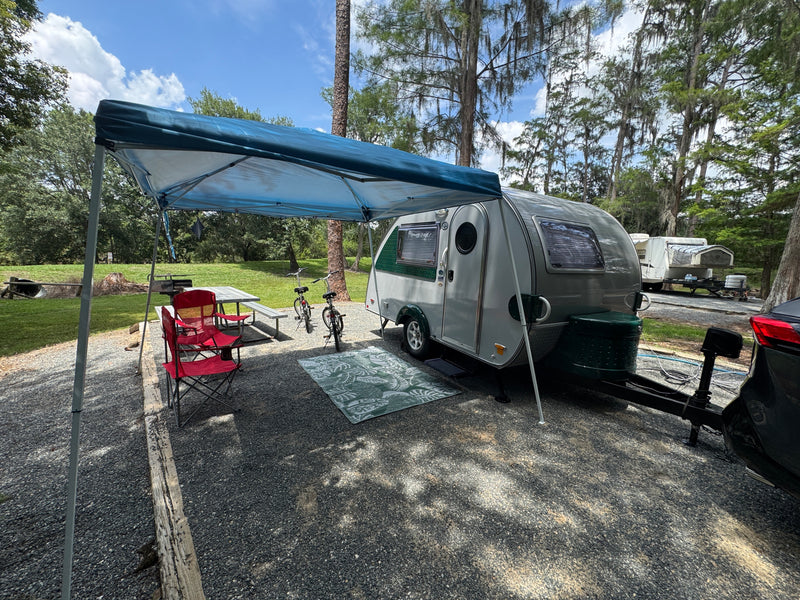 Perfect RV rental campsite setup! A sleek travel trailer, picnic table, and bikes under a canopy on a gravel spot. — photo 9