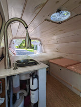 Step into this custom rv rental van: a cozy interior with kitchen sink, bed, wooden walls, and ceiling fan.