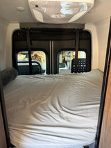 Cozy RV rental sleeping area with a comfortable bed, bolster pillow, and rear windows, perfect for travel.