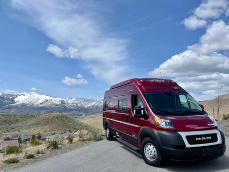 Red Ram ProMaster rv rental parked on a hill, overlooking snow-capped mountains and a residential valley.