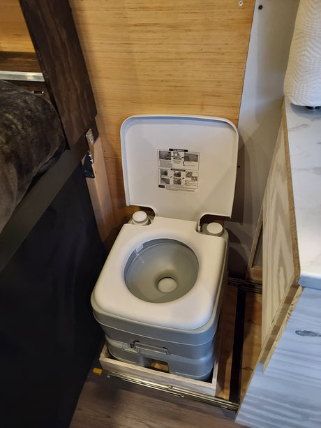 This portable camping toilet, often found in an RV rental, slides out from under a cabinet, with instructions on its lid.