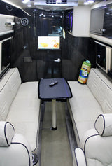 This spacious rv rental interior boasts facing white bench seating, a central table with remote, and an entertainment screen.