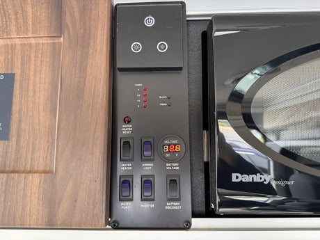 RV rental control panel showing tank levels, voltage display, and switches next to a Danby microwave.