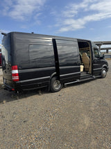 Black camper van, an RV rental, parked on gravel. Its side door is open, showing the cream interior.