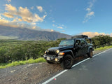 Black Jeep Gladiator w/ rooftop tent on a scenic mountain road. Ideal rv rental for your next outdoor adventure.