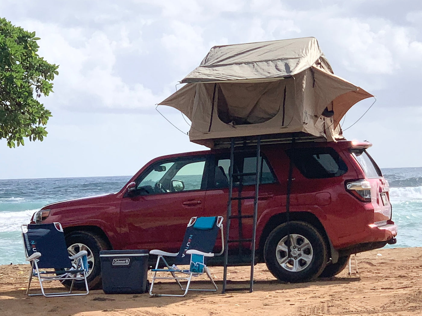 A red SUV with a rooftop tent, ladder, chairs, and cooler set up on a sandy beach. Great for an RV rental camping trip by the ocean. — photo 6