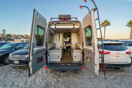 Open doors of an RV rental on a sandy beach, revealing a customized interior perfect for beach camping.