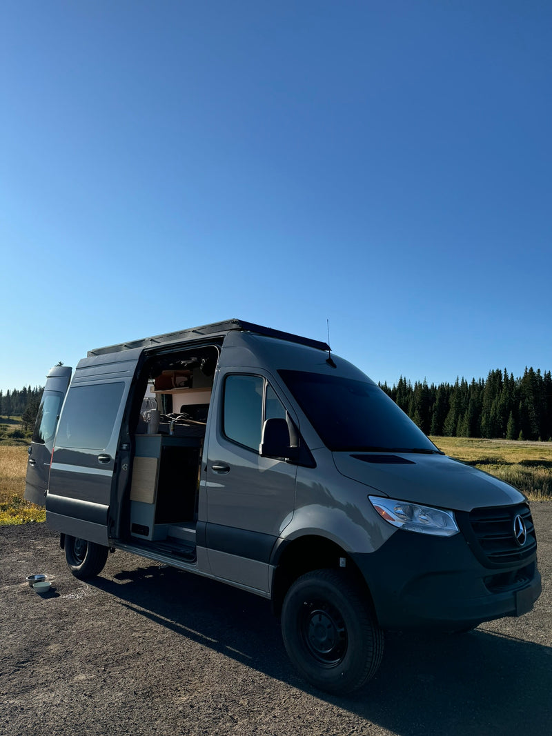  parked on a dirt road beside a blue lake with scenic mountains.|Scenic journey! An RV rental and a dog stand before the Independence Pass sign at the Continental Divide — photo 2