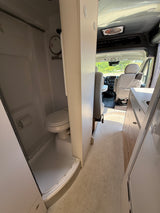 RV rental interior: compact bathroom with toilet & shower on left, leading to kitchen sink & front cabin on right.