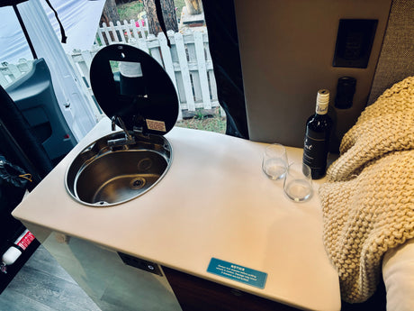 RV rental kitchenette featuring a compact sink with faucet, wine, glasses, and a soft blanket. Ideal for road trips.