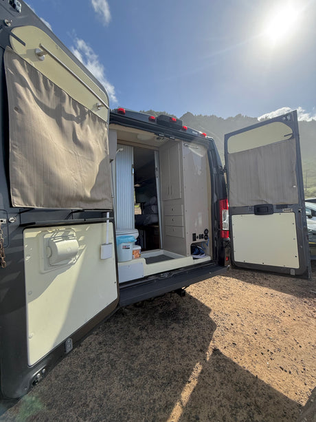 Discover this RV rental: back doors open, revealing a functional interior with a toilet & storage, ready for mountain adventures.