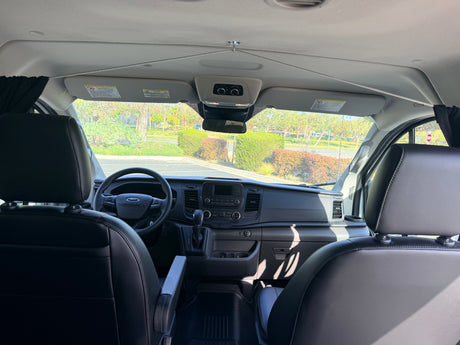 Modern rv rental van interior from the rear, showing the dashboard, steering wheel, front seats, and sunny road ahead.