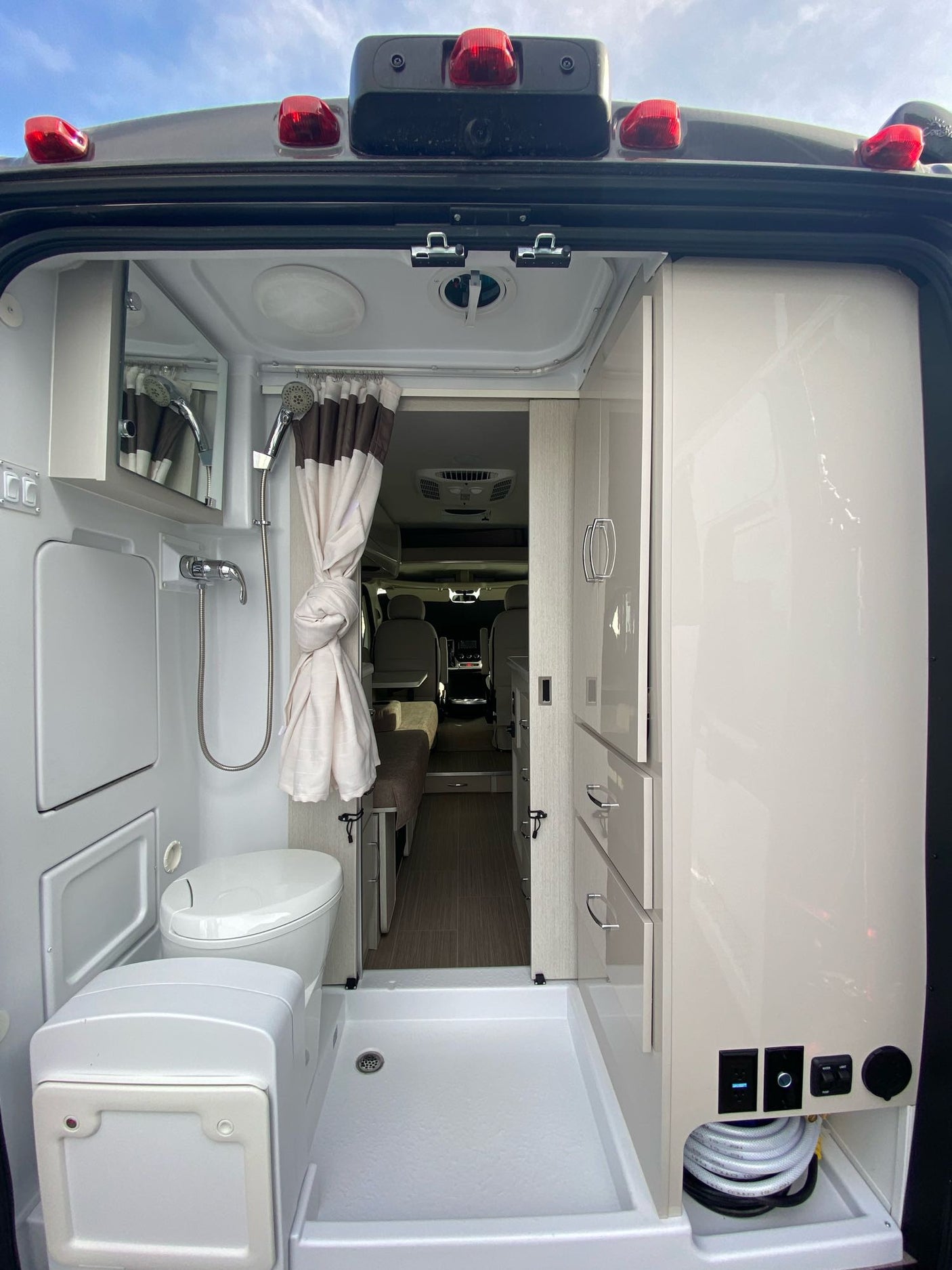 Rear view of an RV rental's compact bathroom with shower, toilet, and storage, showcasing its practical interior design.