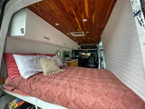 Cozy camper van interior: a comfortable bed, wooden ceiling, and kitchenette. Perfect for an rv rental adventure.