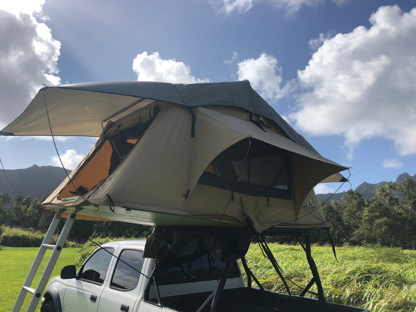 An RV rental alternative: a truck with a rooftop tent set up in a scenic mountain landscape under blue skies.