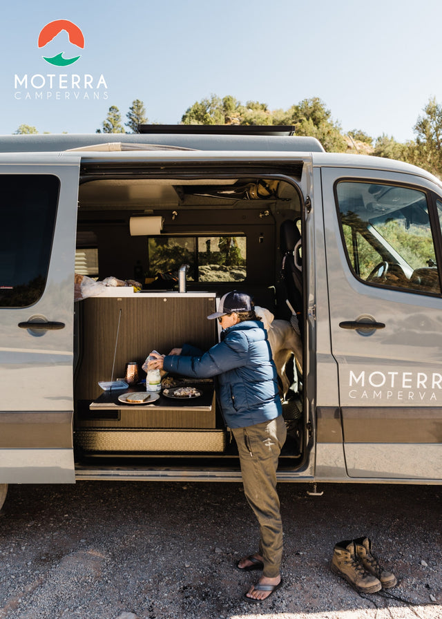 An adventurer cooks outside their grey Moterra RV rental campervan