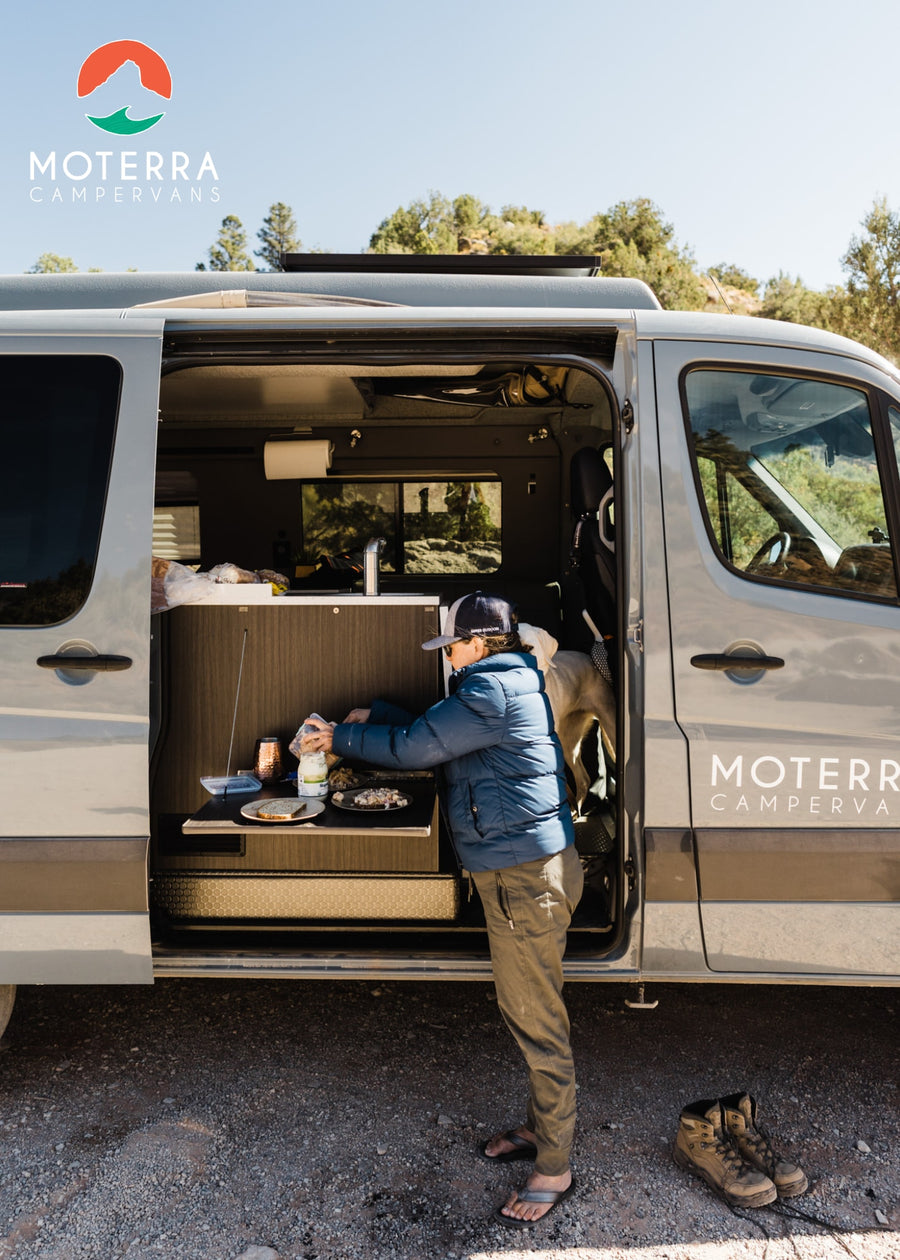 An adventurer cooks outside their grey Moterra RV rental campervan