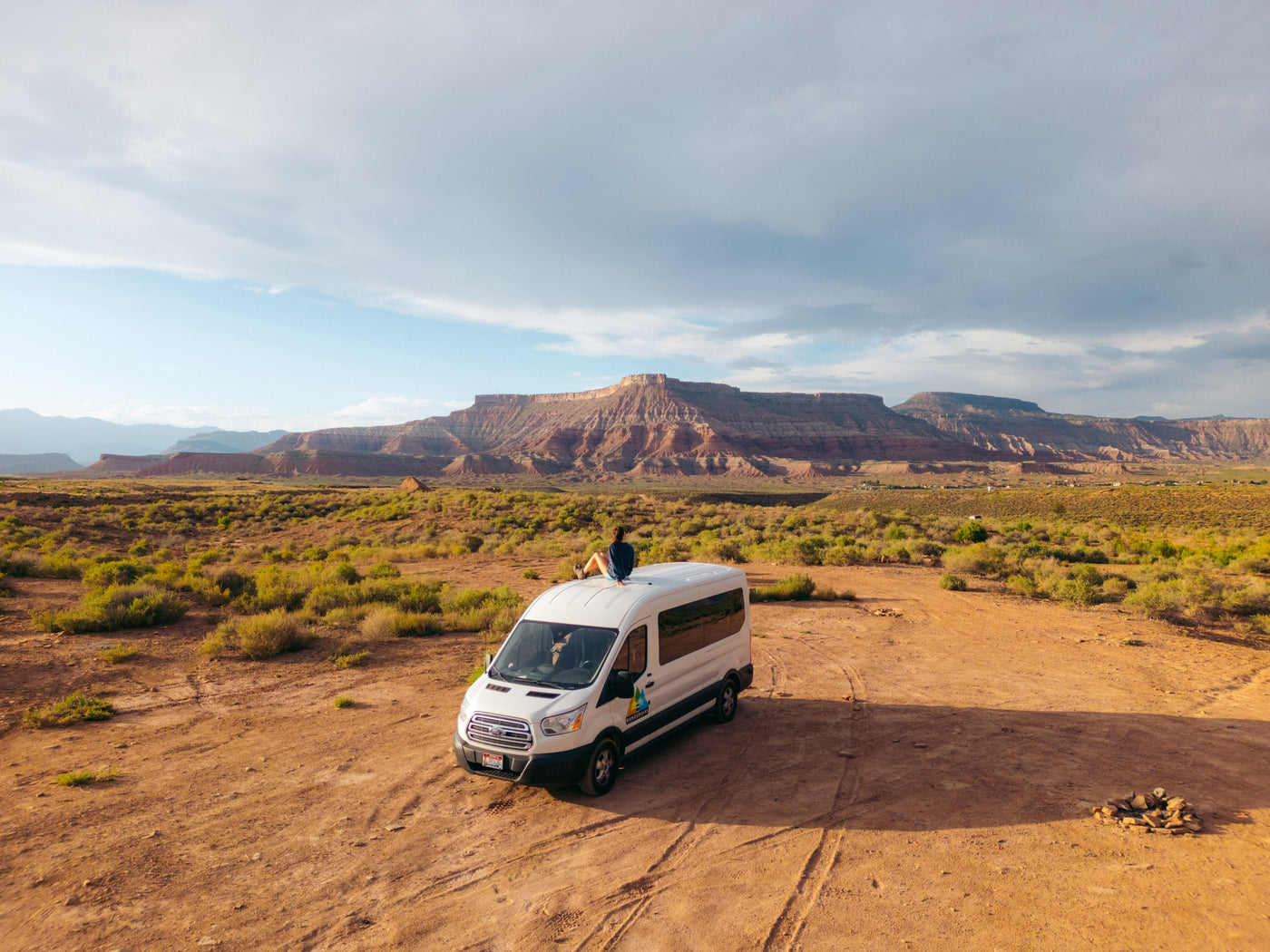 A solo traveler enjoys views from an RV rental van in a vast desert with red rock mountains under a cloudy sky. — photo 12