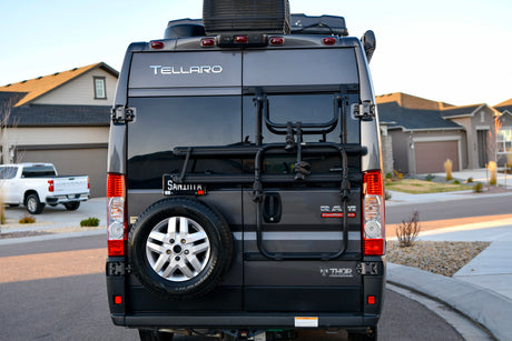 Rear view of a gray Tellaro RV rental, featuring a bike rack and spare tire, parked on a residential street.