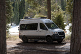 This white Tranquility RV rental camper van is parked in a serene snowy forest, ready for adventure.