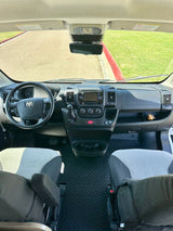 RV rental: Inside a modern camper van cockpit, showing the dashboard, steering wheel, and seats with hexagonal floor mats.