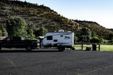 This RV rental and truck are parked, ready for outdoor adventures in a scenic, tree-filled landscape.