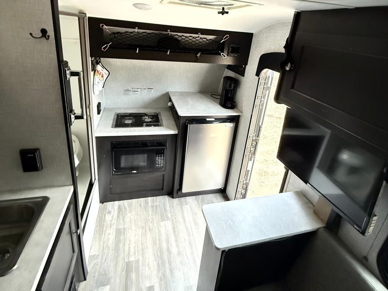  and a small kitchen sink. Ready for adventure!|Explore nature with this Bushwhacker plus RV rental! A sleek white travel trailer sits on a gravel spot — photo 6