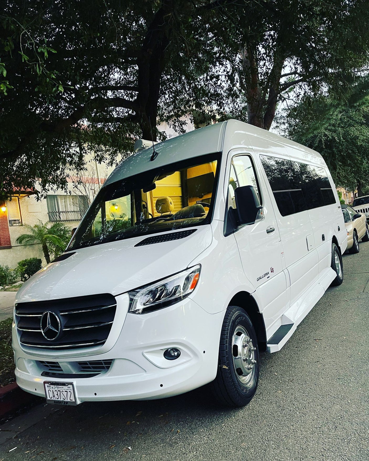White Mercedes-Benz Sprinter RV rental, a sleek camper van parked on a residential street lined with trees.