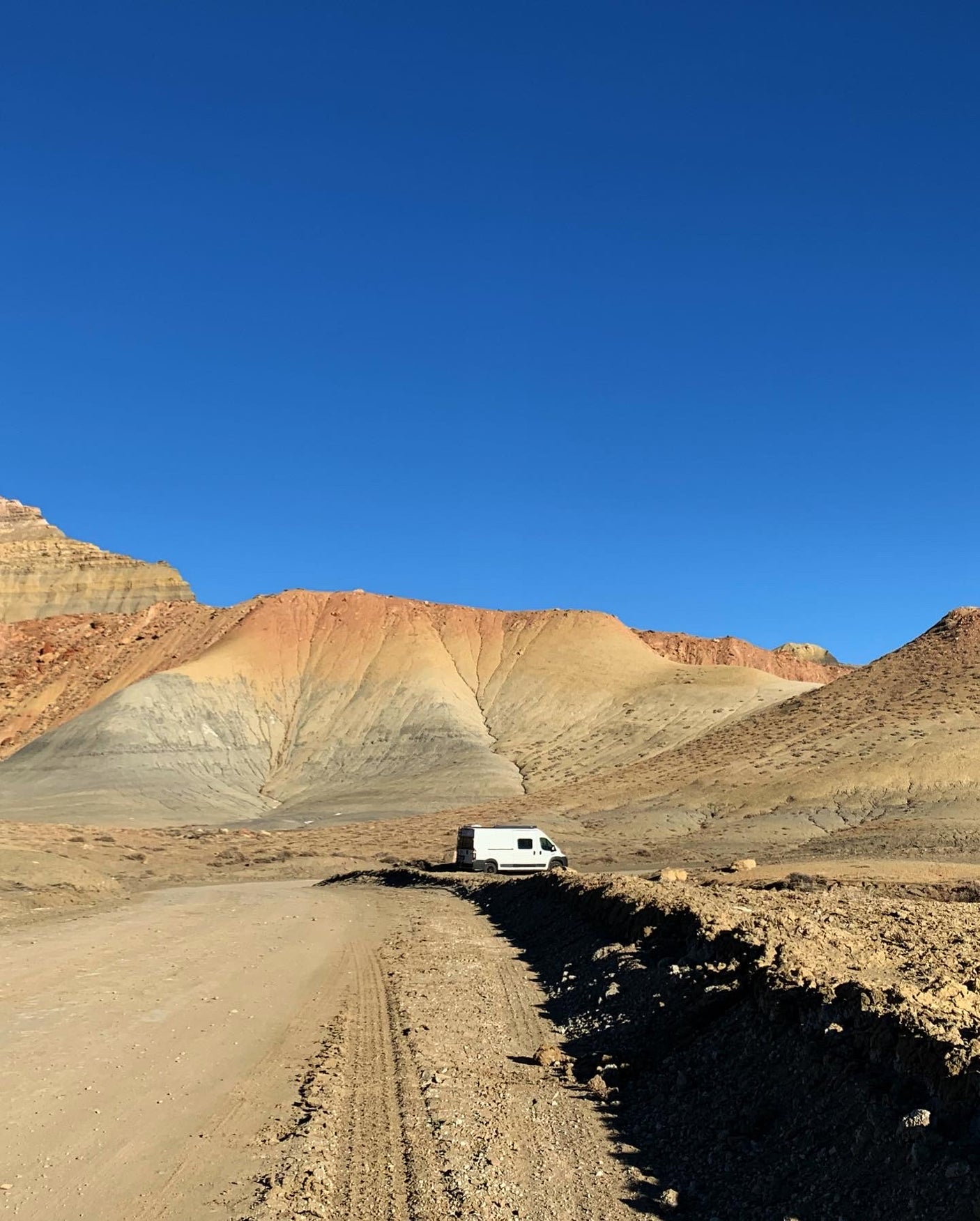 Vibrant desert mountains frame an rv rental on a dusty road under a clear sky. Perfect for remote adventure travel.
