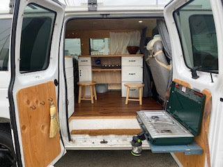 This RV rental offers a glimpse inside a custom camper van with a cozy kitchen and outdoor cooking setup.