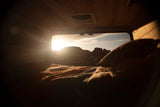 Wake up to desert views from your RV rental! Cozy bed inside, with sun over mountains through the window.