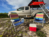 Enjoying an RV rental setup: a truck with rooftop tent, chairs, cooler, & snacks on a sandy campsite.